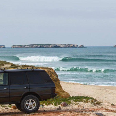 A four-by-four parked above a sandy beach, with waves breaking offshore