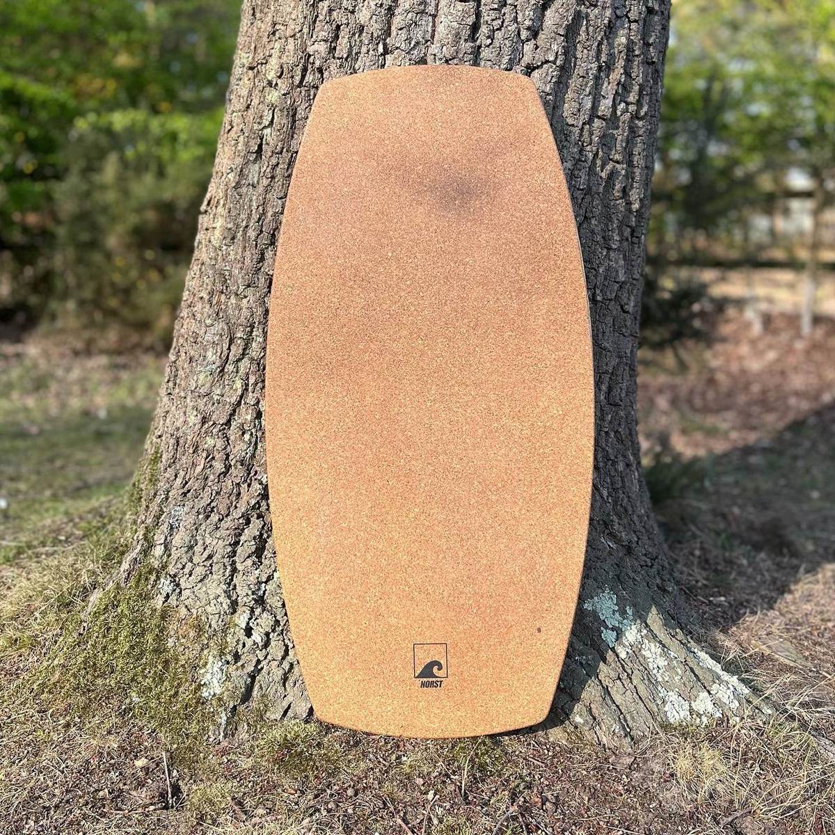 A Norst board stood against a tree, cork deck and logo facing out.