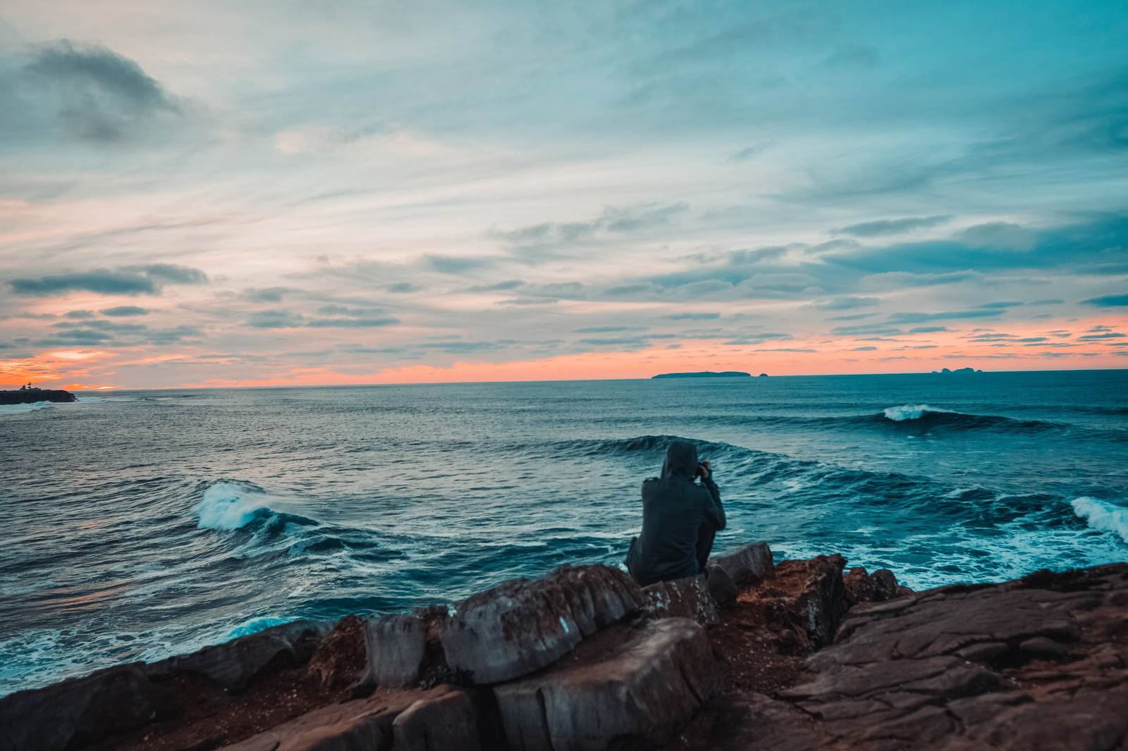 A person on coastal rocks at dusk, watching waves at Peniche, Portugal