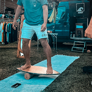 A barefoot rider balancing on a Norst board and roller on a mat