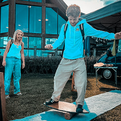 A rider in a blue hoodie balancing on a Norst board and roller at an outdoor event