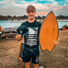 A rider holding a Norst Surf Balance Board beside a lake