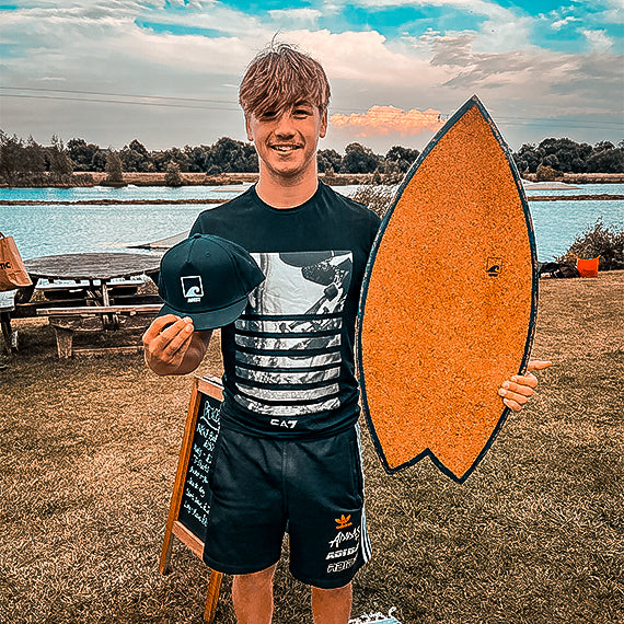 A rider holding a Norst Surf Balance Board beside a lake