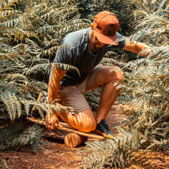 A man kneeling to set the Norst Surf Balance Board on its roller among ferns