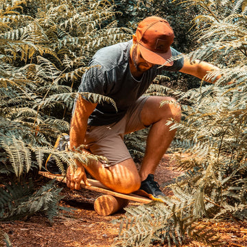 A man kneeling to set the Norst Surf Balance Board on its roller among ferns