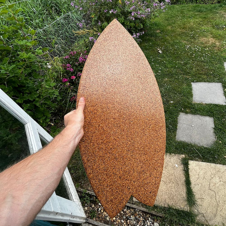 A hand holding a Norst Surf Balance Board, cork top deck, in a garden