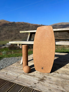 A Norst Freestyle Balance Board with a cork roller and cork ball on decking, hills behind