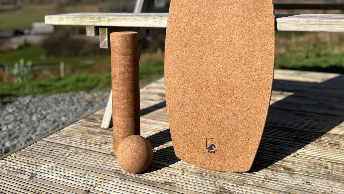 A Freestyle board, cork roller and cork ball on a wooden deck outdoors.