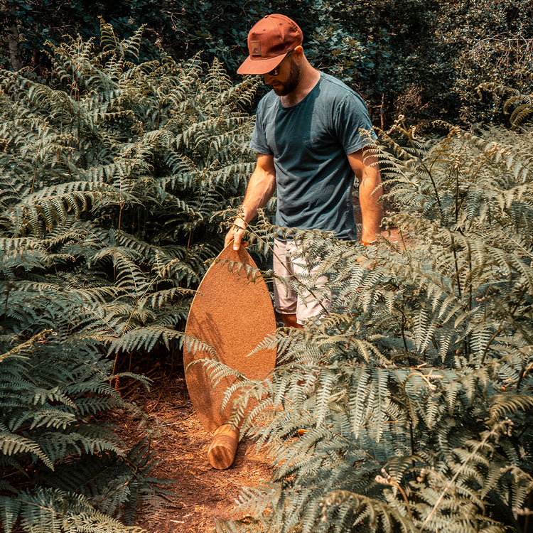 A man carrying a Norst Surf Balance Board through ferns
