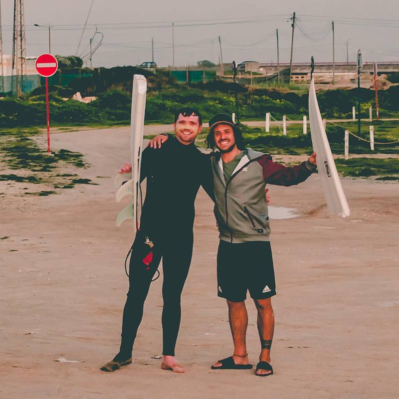 Two friends holding surfboards on a beach.